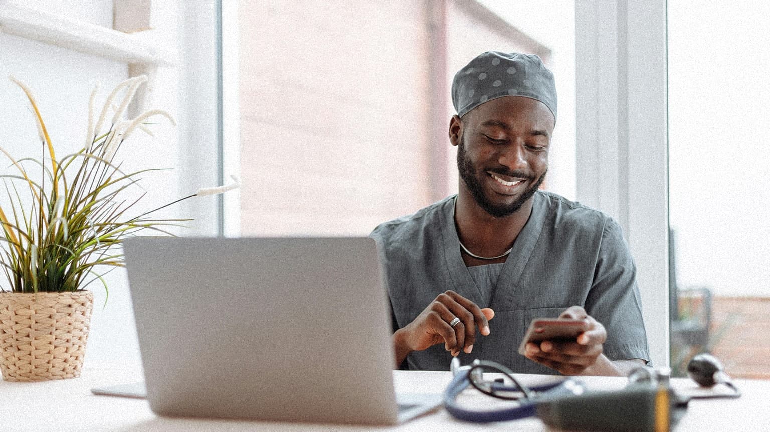 Doctor looking at desk smiling while looking down at his phone